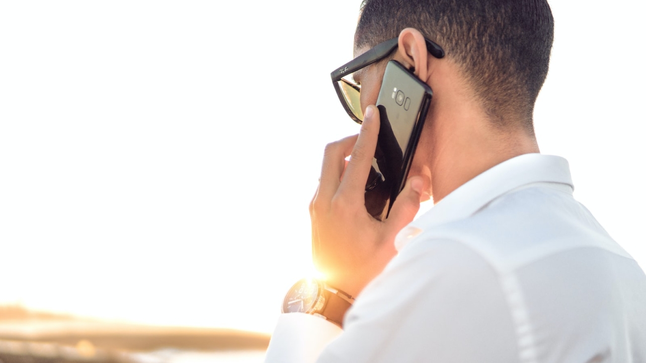 man holding smartphone standing in front of calm body of water