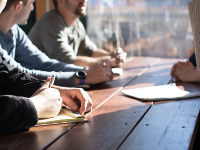 people sitting on chair in front of table while holding pens during daytime