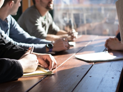 people sitting on chair in front of table while holding pens during daytime